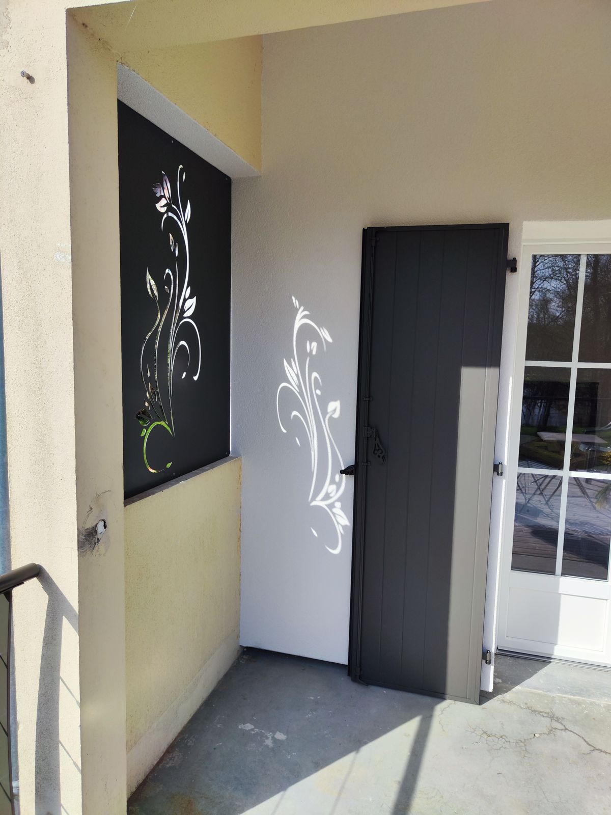 Panneau brise-vue en acier découpé à motif floral à côté d'une porte d'entrée