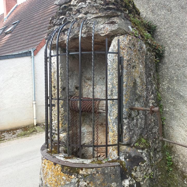 Grille en fer forgé en forme de cage protégeant un puits ancien en pierre