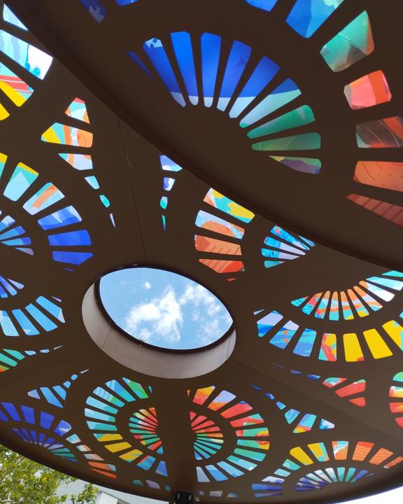 Oculus central d'une ombrière en acier découpé entouré de motifs colorés