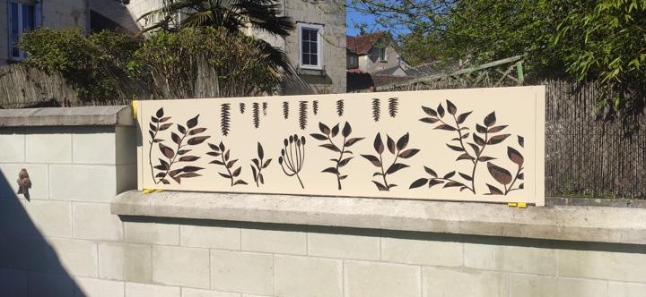 Panneau en acier laqué blanc découpé de motifs botaniques posé sur un muret de jardin