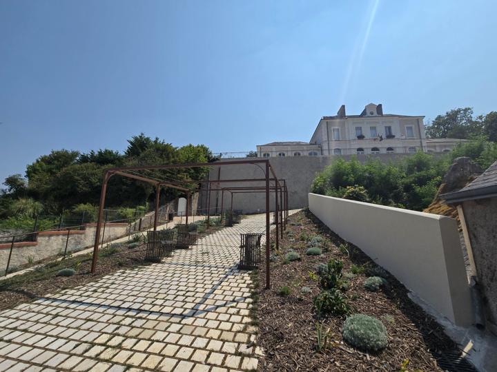 Pergola en acier patiné au-dessus d'une allée pavée montant vers la mairie de Véretz
