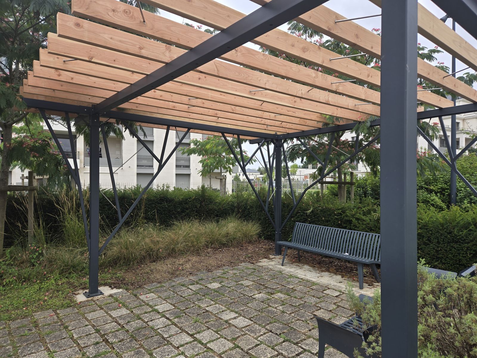 Pergola en forme d'arbre en acier peint, inox et lames de bois au-dessus d'un espace de repos dans un parc