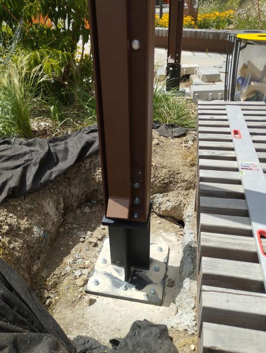 Pied de poteau d'ombrière en acier fixé sur platine dans une fouille avant finition