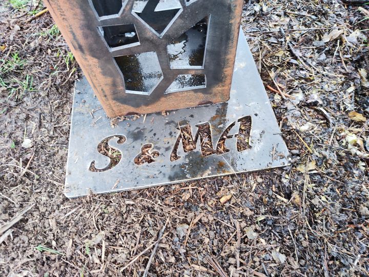 Platine de pied de brasero en acier découpée des lettres S&MA, posée au sol