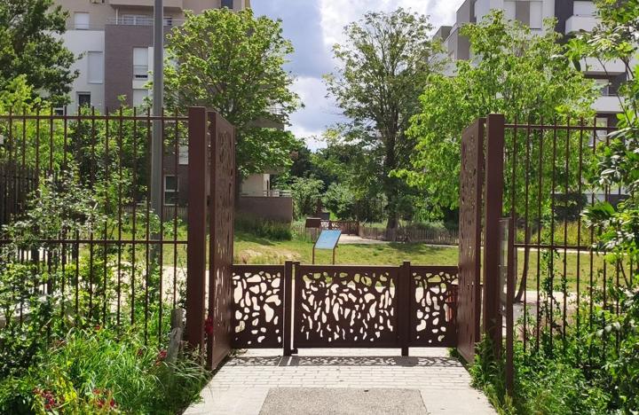 Portillon en acier corten découpé à motifs organiques entre deux grilles dans un jardin