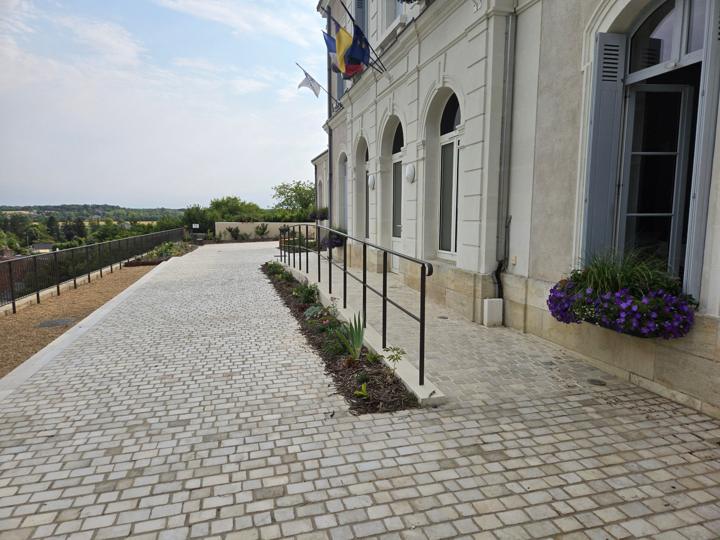 Main courante métallique bordant une rampe d'accès pavée le long de la façade de la mairie de Véretz