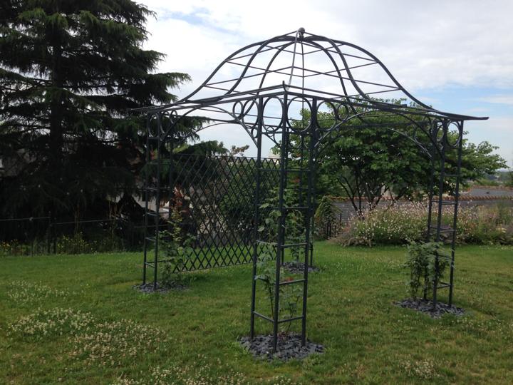 Tonnelle en fer forgé avec dôme ornemental et treillage dans un jardin