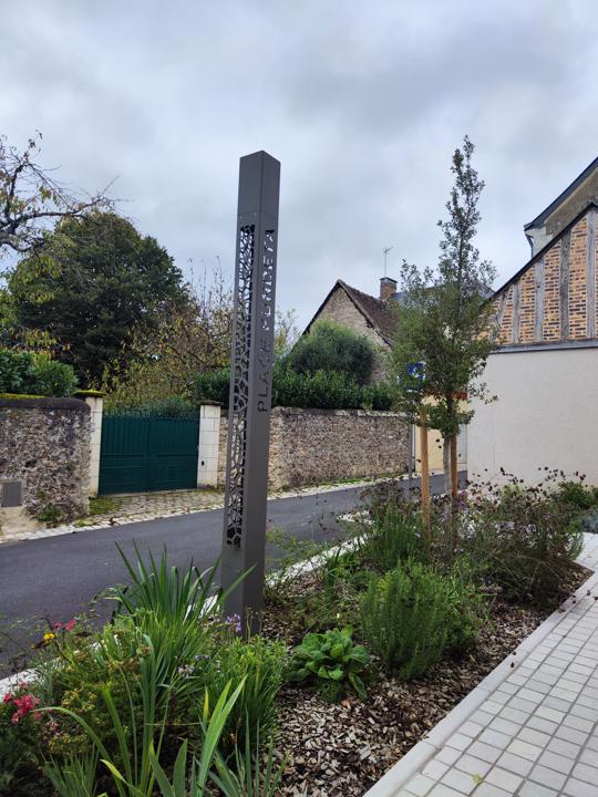 Totem en acier intégré dans les massifs plantés d'une place de village
