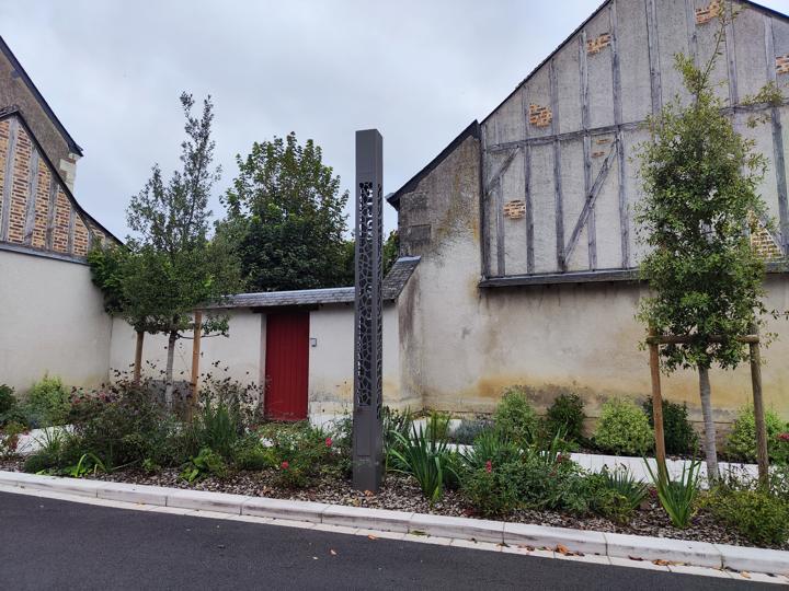 Totem en acier à motifs géométriques découpés au milieu d'un aménagement paysager de place
