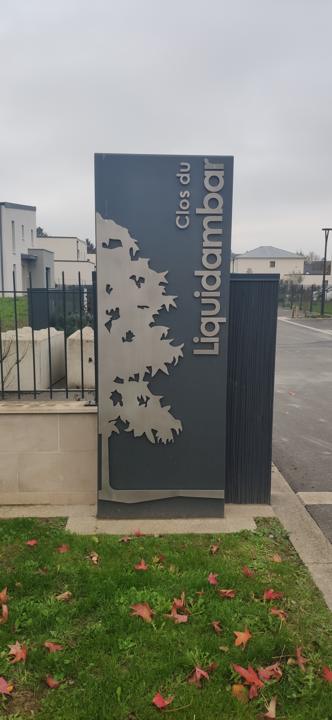 Totem de quartier en acier sombre ajouré d'un motif végétal